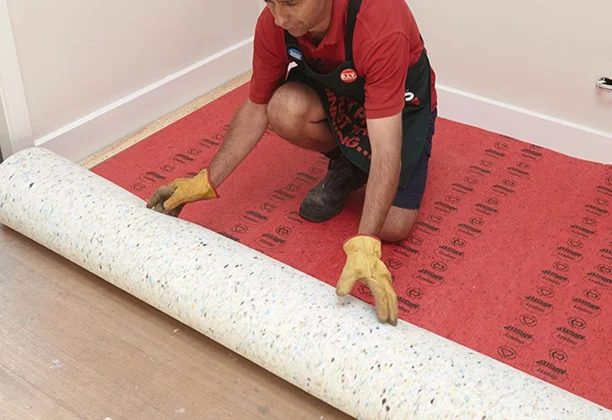 Carpet installer insalling red colored underlay for wall to wall carpet in a room